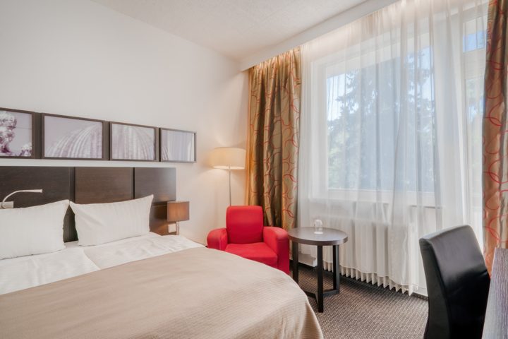 Einzelzimmer im Waldhotel mit Bett, Schreibtisch und rotem Sessel