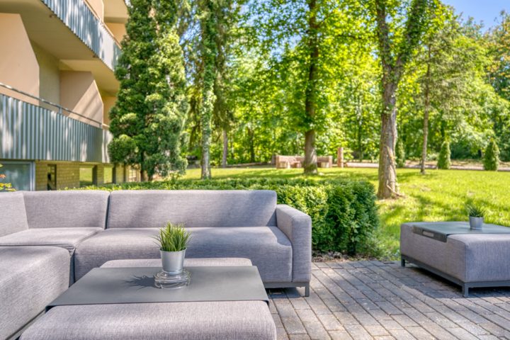 Graue Loungemöbel auf der Terrasse mit Blick in den grünen Hotelgarten